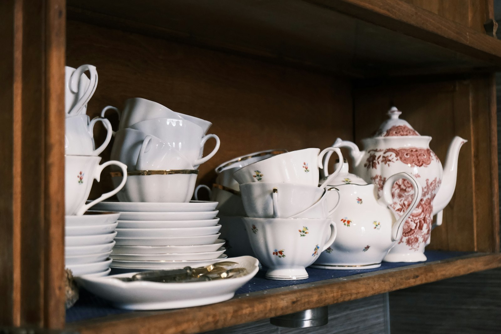 Tazas, platos y una tetera de loza fina guardados en un mueble de madera