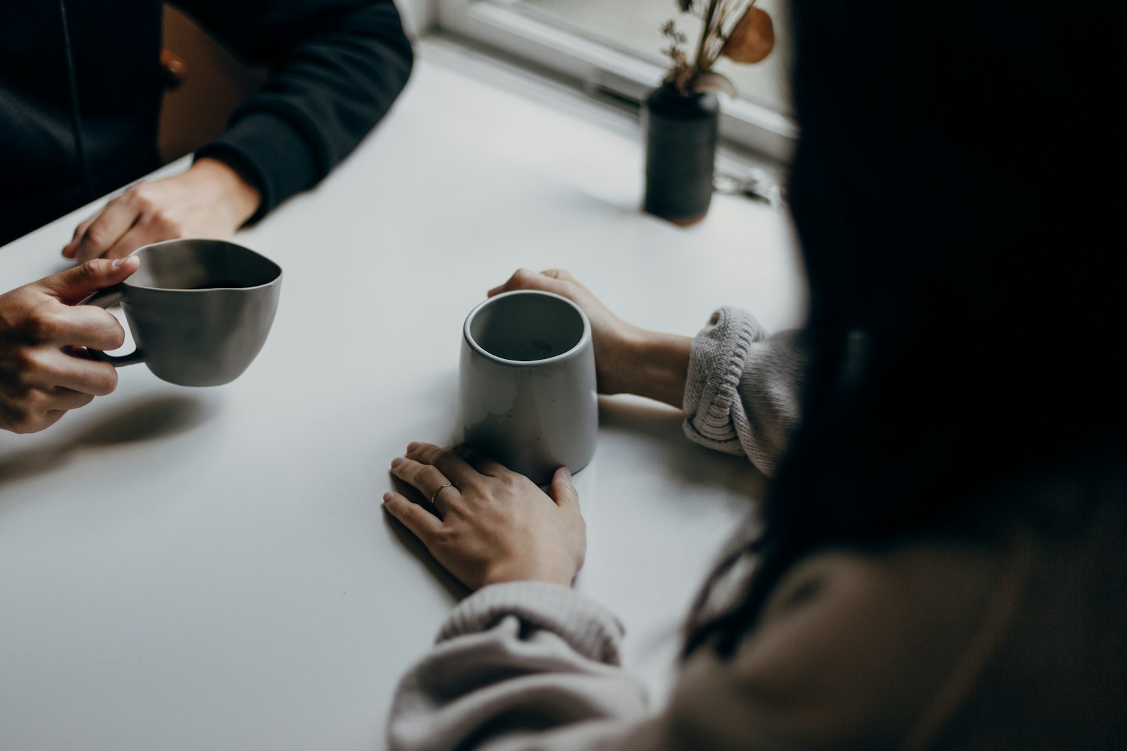 Dos personas sentadas frente a frente en una mesa, cada una con su taza, sin tocarse